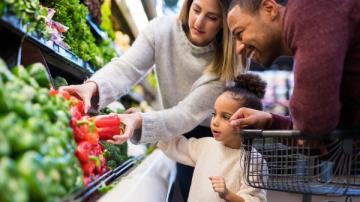 A family of a mom, dad and little girl look at red bell peppers in a grocery store