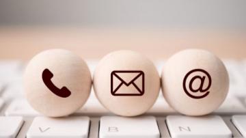 Three wooden balls bearing the symbols for a phone, email and social media at symbol.