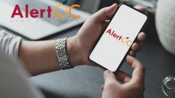 A person looks at their mobile phone with the Alert OC logo