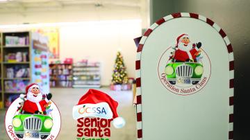 The Operation Santa Claus and Senior Santa and Friends logos sit in the bottom left corner. Behind them is some of the storefront. On the right is a mailbox with the Operation Santa Claus Logo. 