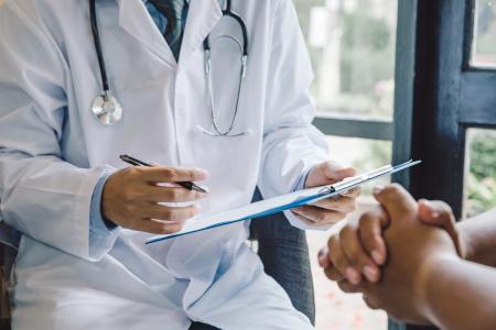 Doctor facing a patient and writing notes on a clipboard